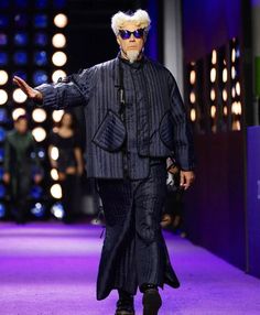 a man with white hair and sunglasses walking down a runway