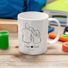 a white coffee mug sitting on top of a wooden table next to markers and pens