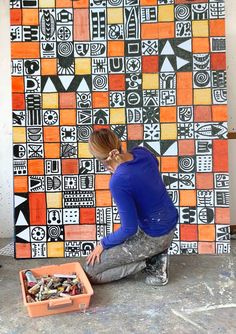 a woman sitting on the ground in front of a wall covered with colorful squares and shapes