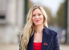 a woman with long blonde hair wearing a blue jacket and red top smiling at the camera