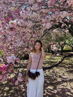 a woman standing under a tree with pink flowers