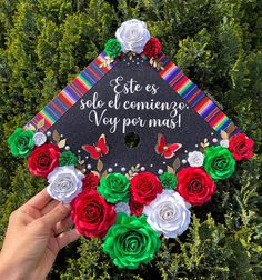 a graduation cap decorated with flowers and writing on the top is being held up by someone's hand