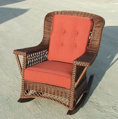 a wicker rocking chair with an orange cushion sits in the sand at the beach