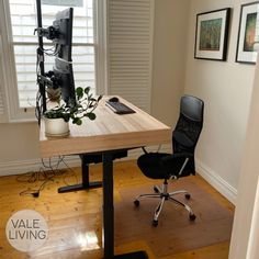 a desk with a computer monitor, keyboard and plant on it in front of a window