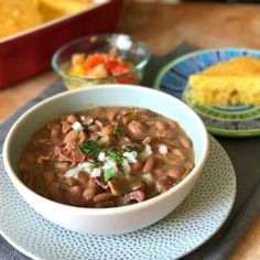 a white bowl filled with beans on top of a plate next to cornbreads