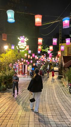 a woman walking down a street with lots of lights hanging from the ceiling above her