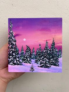 a hand holding up a small card with trees in the snow and a pink sky