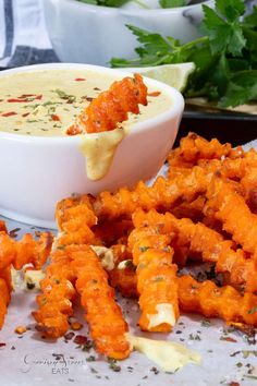 a bowl of dip and some fried food on a table with other foods in the background