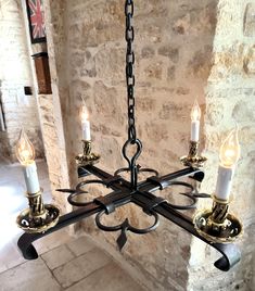 a chandelier with five candles hanging from it's center, in front of a stone wall