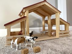 several toy farm animals in front of a wooden stable with hay on the floor and two horses