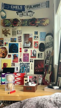 a desk with various items on it in front of a wall full of posters and pictures