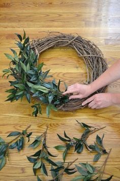 someone is making a wreath out of twigs and greenery on the floor with their hands