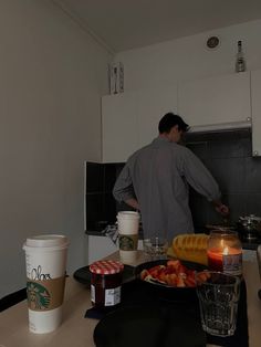 a man standing in a kitchen preparing food on top of a counter next to cups