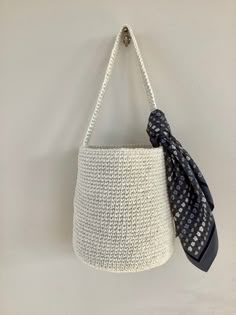 a crocheted purse hanging on a wall with a scarf tied to the handle