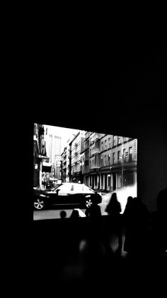 black and white photograph of people watching a car go by