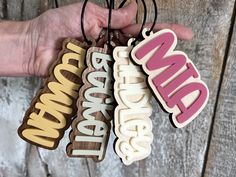 a hand holding four wooden name tags with the word grandma on them in different colors