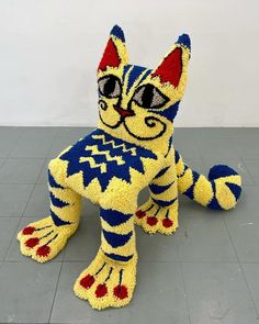 a cat made out of yarn sitting on top of a tile floor next to a wall