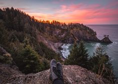 a person's feet resting on the edge of a cliff overlooking the ocean at sunset