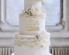 a wedding cake with white flowers and gold lettering