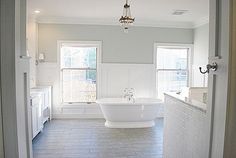 a large white bathroom with a chandelier hanging from the ceiling and two windows