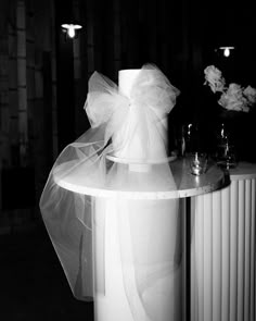 a table topped with a white cake covered in a sheer ribbon and two wine glasses sitting on top of it