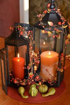 two lit candles sitting next to each other on top of a table with leaves and berries