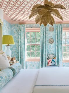 a bedroom with blue and white wallpaper, ceiling fan and bed in front of two windows