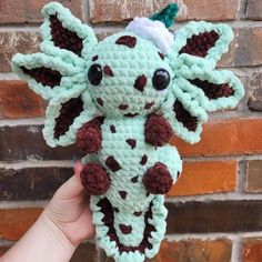 a crocheted giraffe is held up in front of a brick wall