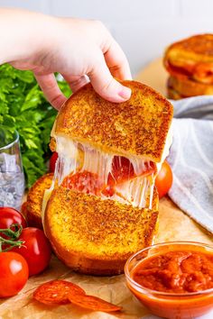 someone is holding up a sandwich with cheese and tomato sauce on the table next to some tomatoes