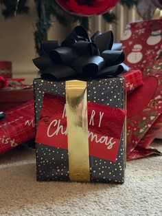 a present wrapped in black and gold paper with a ribbon tied around it, sitting on the floor next to christmas presents