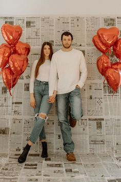 a man and woman standing next to each other in front of red heart shaped balloons