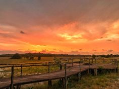 the sun is setting over an open field with wooden walkways leading to some water