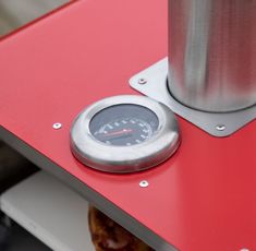 a red table with a gauge on it and a metal object next to it that looks like a coffee pot