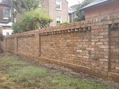 a brick fence in front of a house with grass on the ground and buildings behind it