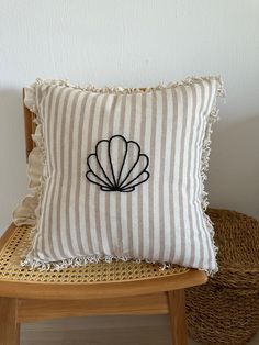 a pillow with a shell embroidered on it sitting on a chair next to a wicker basket