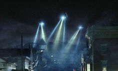 three spotlights shine brightly over a city street at night