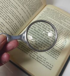 a hand holding a magnifying glass over an open book