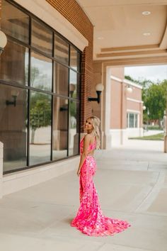 a woman standing in front of a building wearing a bright pink dress and looking off to the side