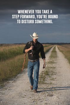 a man walking down a dirt road with a cowboy hat on