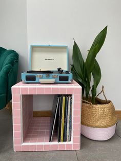 a record player sitting on top of a pink shelf next to a potted plant