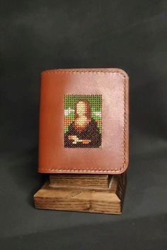 a small wallet with a picture of jesus on the front and side, sitting on top of a wooden stand