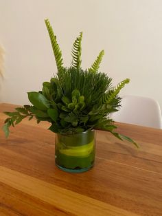 a green vase filled with plants on top of a wooden table