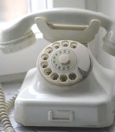 an old white phone sitting on top of a tiled floor next to a window and telephone cord