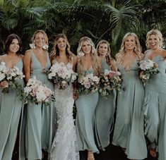 a group of women standing next to each other wearing dresses and holding bouquets in their hands