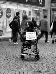 a woman sitting in a wheel chair holding a sign