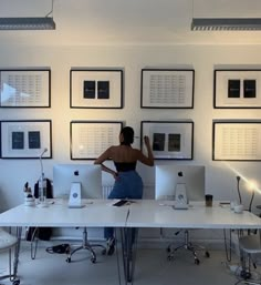 a woman standing in front of two computer monitors on a desk with multiple pictures above her