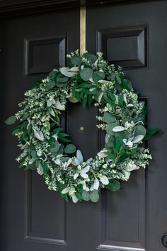 a wreath is hanging on the front door with green leaves and greenery around it