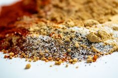 several different types of spices and seasonings on a white surface with red, yellow, and blue colors