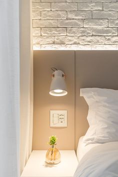 a bed with white sheets and pillows next to a wall light that is turned on