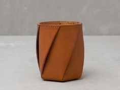 a brown leather vase sitting on top of a white table next to a gray wall